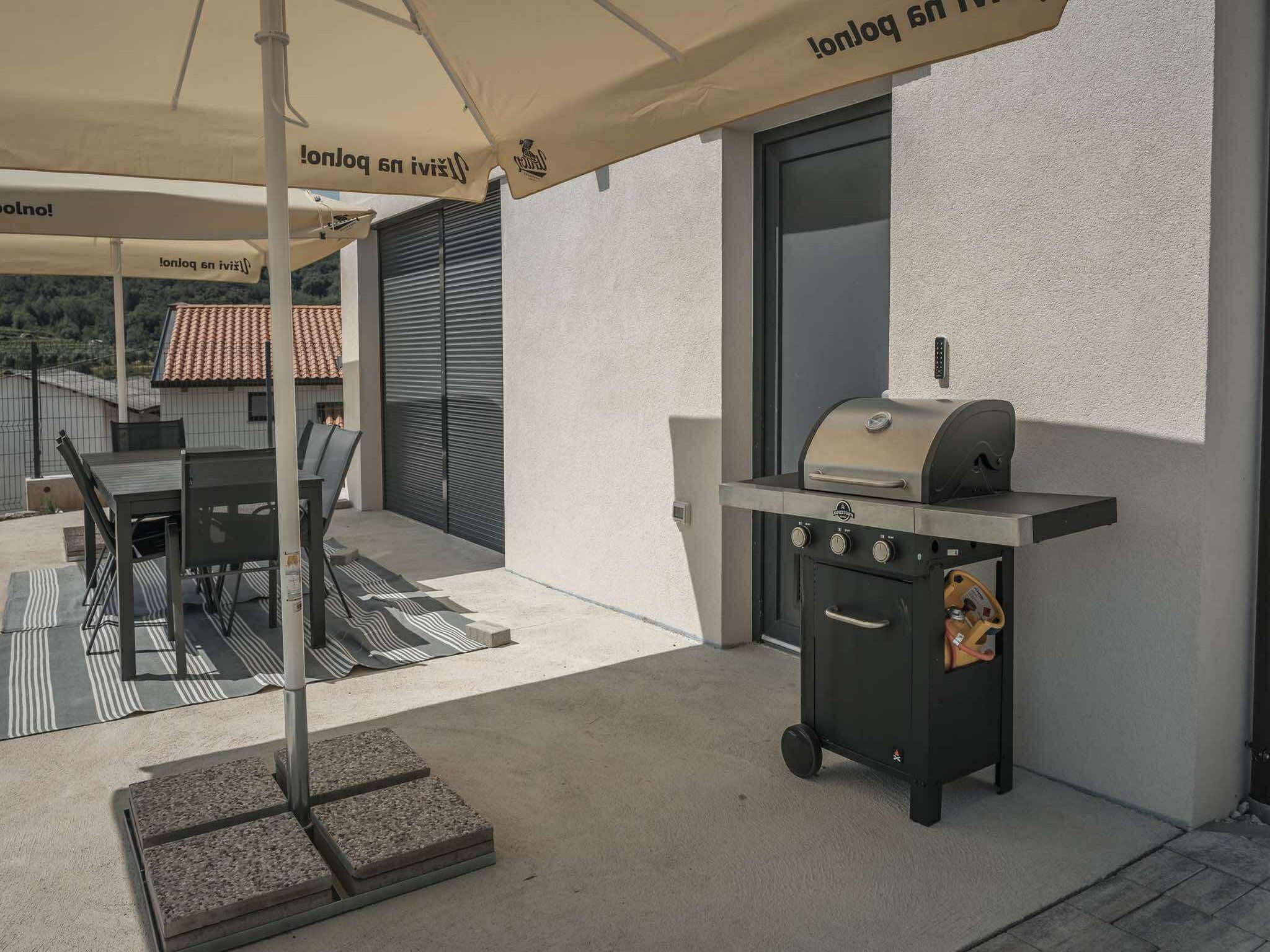 An outdoor patio with a grill, a table, and chairs.