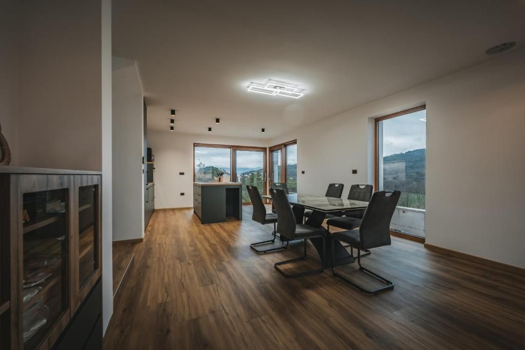 Un comedor moderno con piso de madera, una mesa con sillas y grandes ventanales que ofrecen vistas al exterior.
