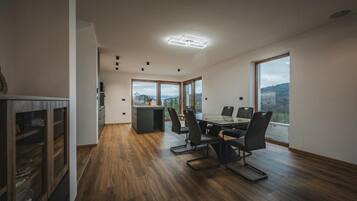 Un comedor moderno con piso de madera, una mesa con sillas y grandes ventanales que ofrecen vistas al exterior.