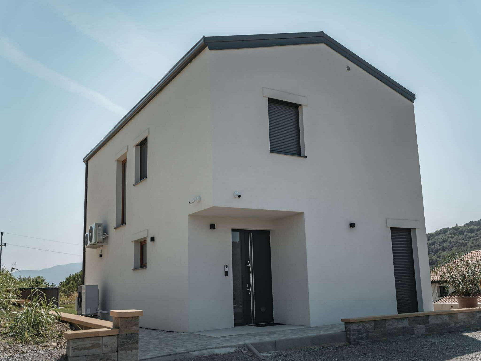 Una casa moderna de dos pisos con techo plano, una puerta principal y dos ventanas en la planta baja.