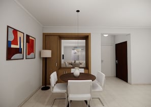 Un comedor con una mesa redonda, sillas blancas y un centro de mesa con un florero. Hay pinturas abstractas en la pared y una lámpara de pie alta.