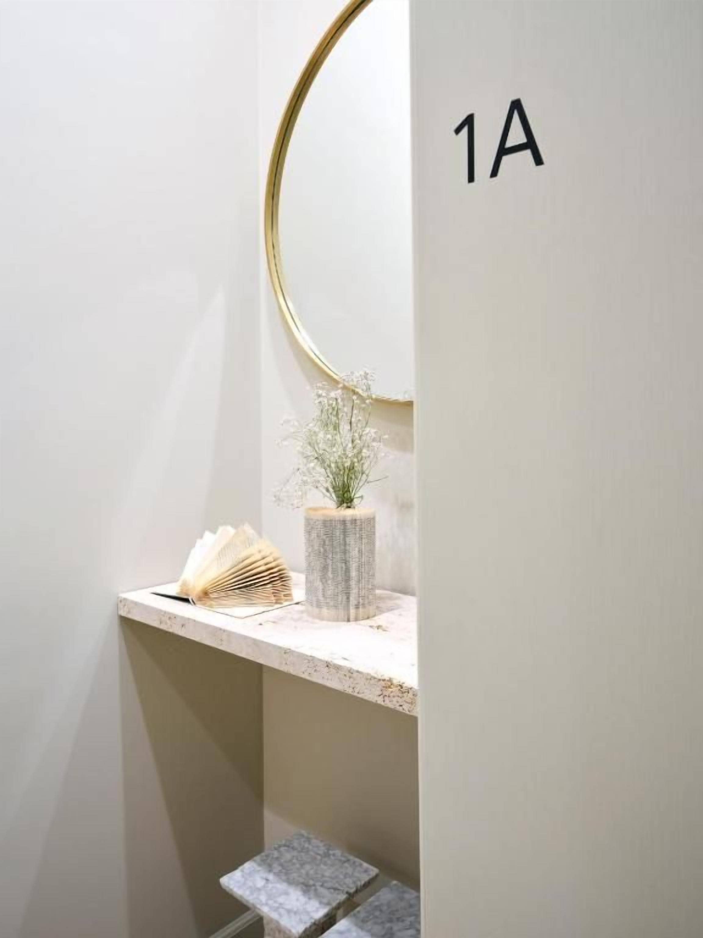 Un baño con tocador, espejo, planta en maceta y señal con número.
