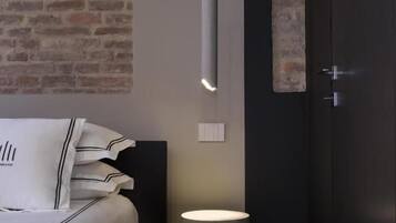 Quarto com cama, mesa de cabeceira e luminária suspensa.