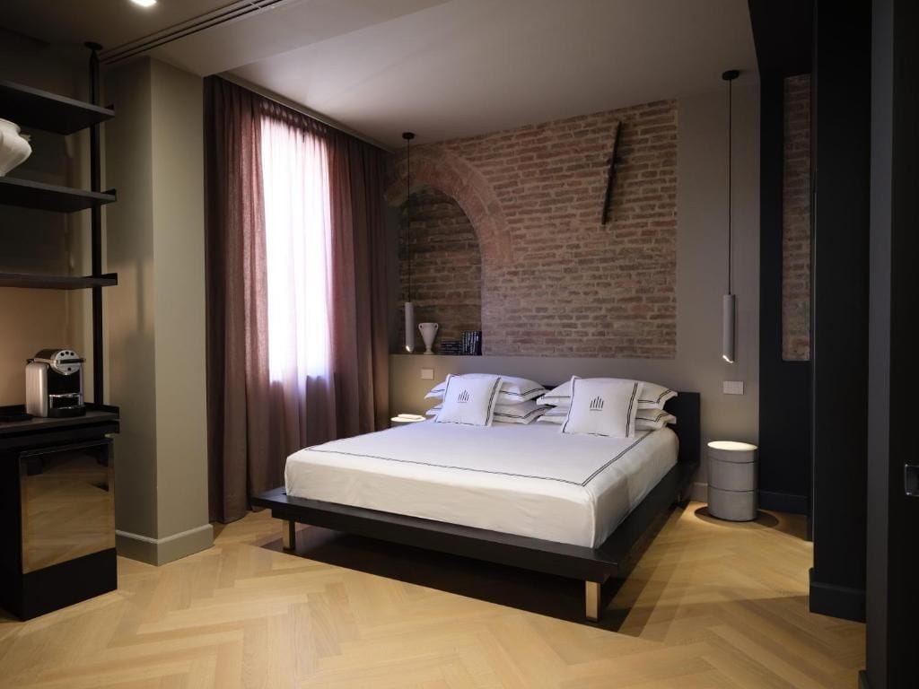 A modern bedroom with a brick wall, a bed with white bedding, a bedside table, and a hanging light fixture.