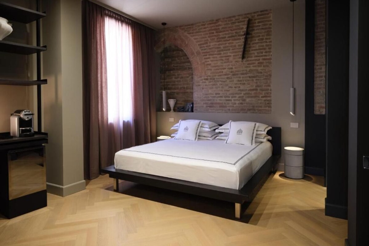 Un dormitorio moderno con pared de ladrillo, una cama con ropa blanca, una mesita de noche y una lámpara colgante.