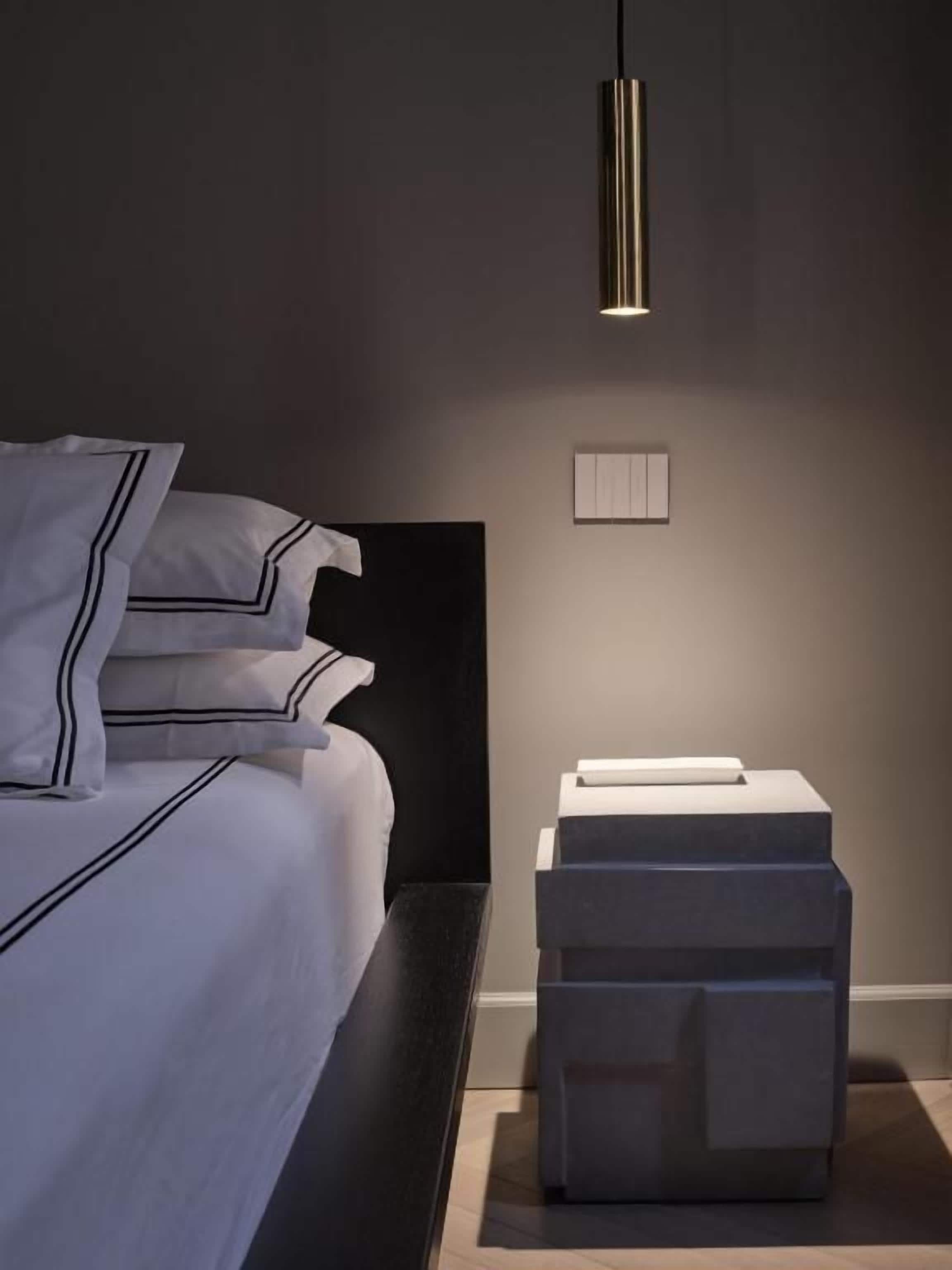 Une chambre moderne avec un lit, des tables de chevet et un luminaire fixé au mur.