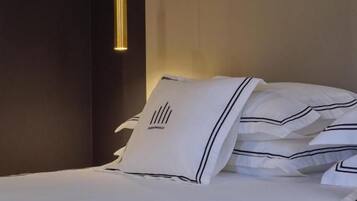 Een netjes opgemaakt bed met witte lakens en gestreepte kussens, een wandlamp en een donker hoofdbord.