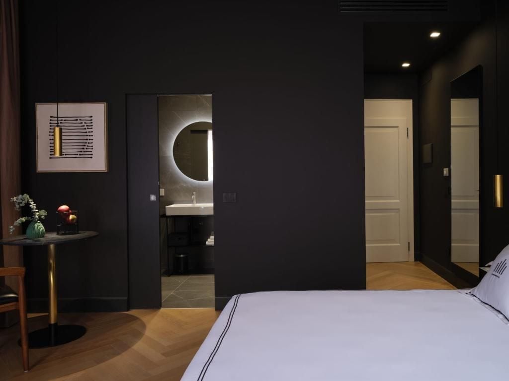 Une chambre à coucher moderne avec un grand lit, un petit miroir rond et une œuvre d’art encadrée accrochée au mur.