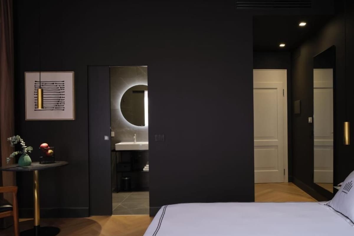 Un dormitorio moderno con una cama grande, un espejo redondo pequeño y una obra de arte enmarcada en la pared.