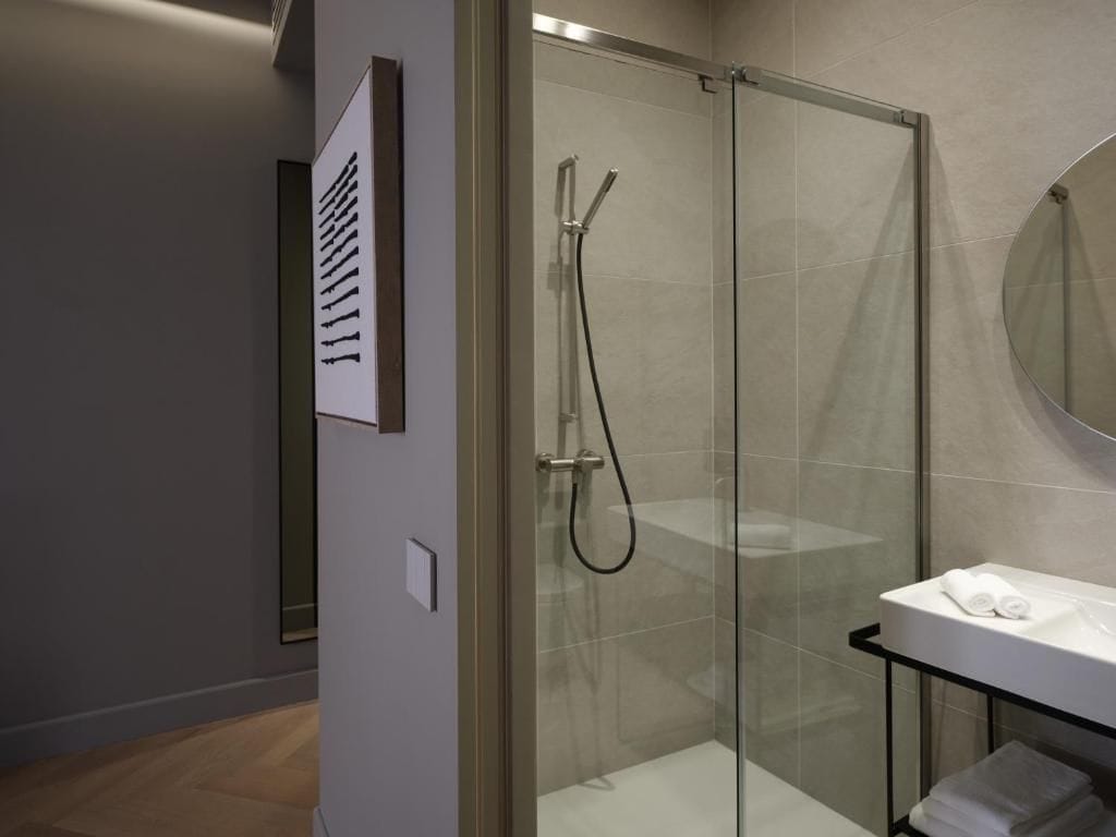 Un baño moderno con ducha envuelta en vidrio, un lavamanos blanco y un espejo.