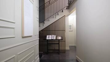 Un pasillo con una escalera, una estantería y una puerta con ventanal.