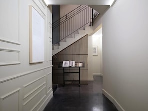 Un pasillo con una escalera, una estantería y una puerta con ventanal.