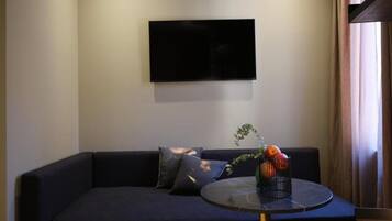 Una sala de estar moderna con un sofá oscuro, un televisor de pantalla plana montado en la pared y una pequeña mesa redonda con un jarrón de flores.