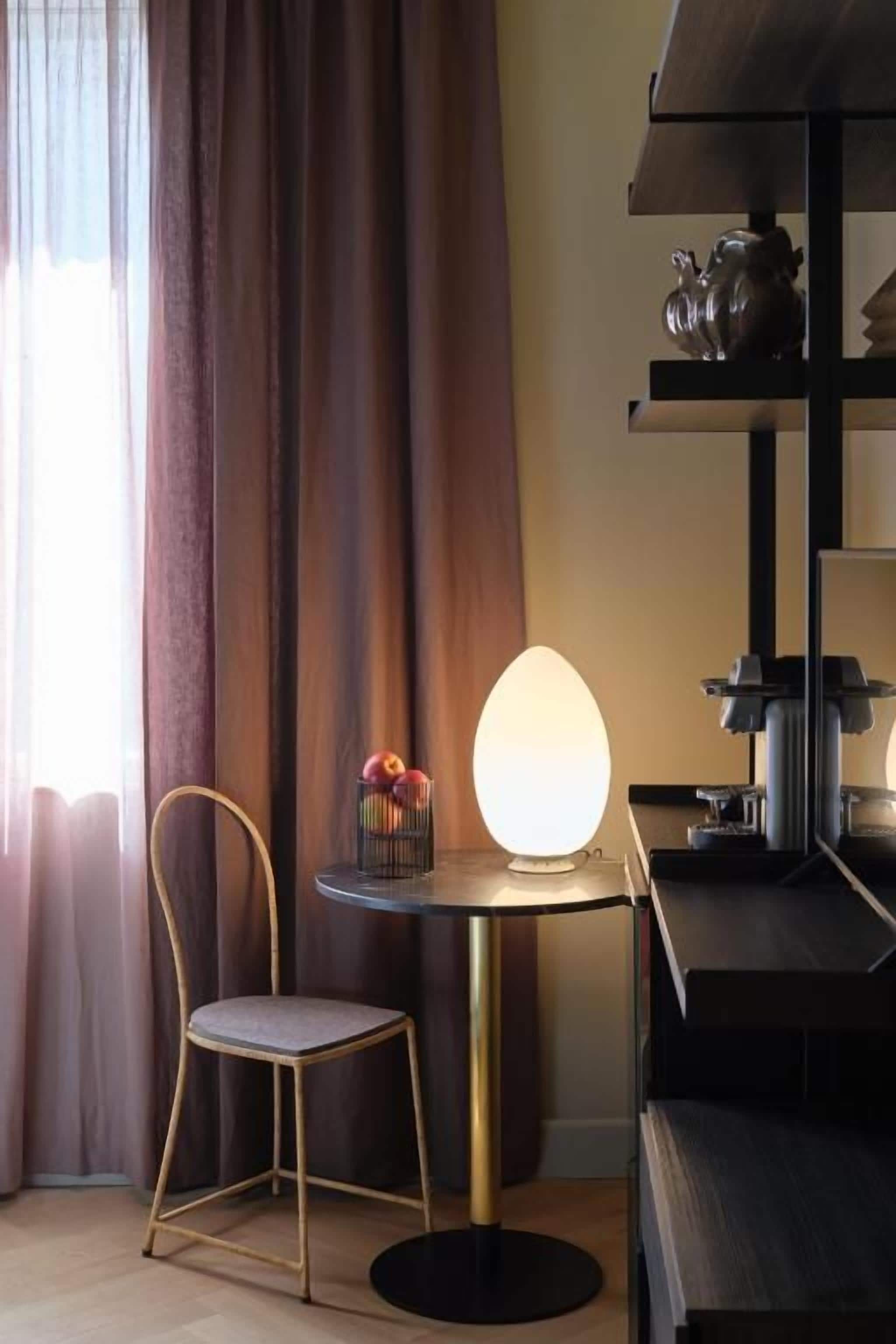 Una habitación con una mesa redonda, una silla, una lámpara y un estante con adornos.