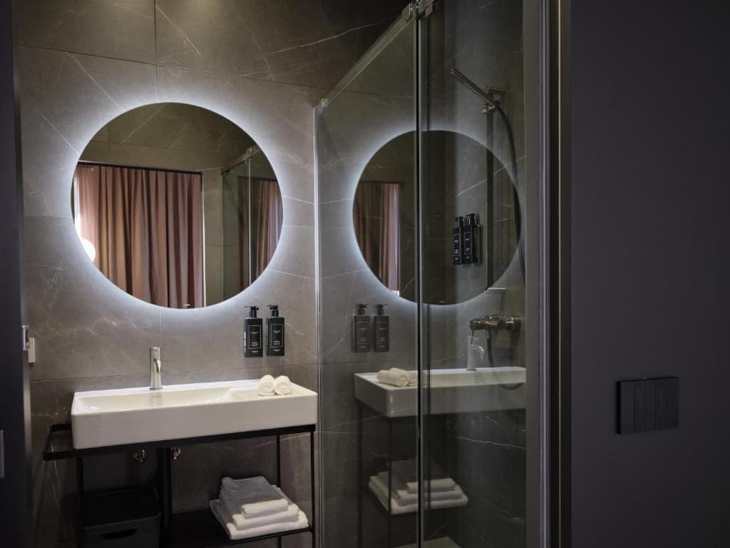A modern bathroom with a glass-enclosed shower, a vanity with a sink, and two round mirrors.
