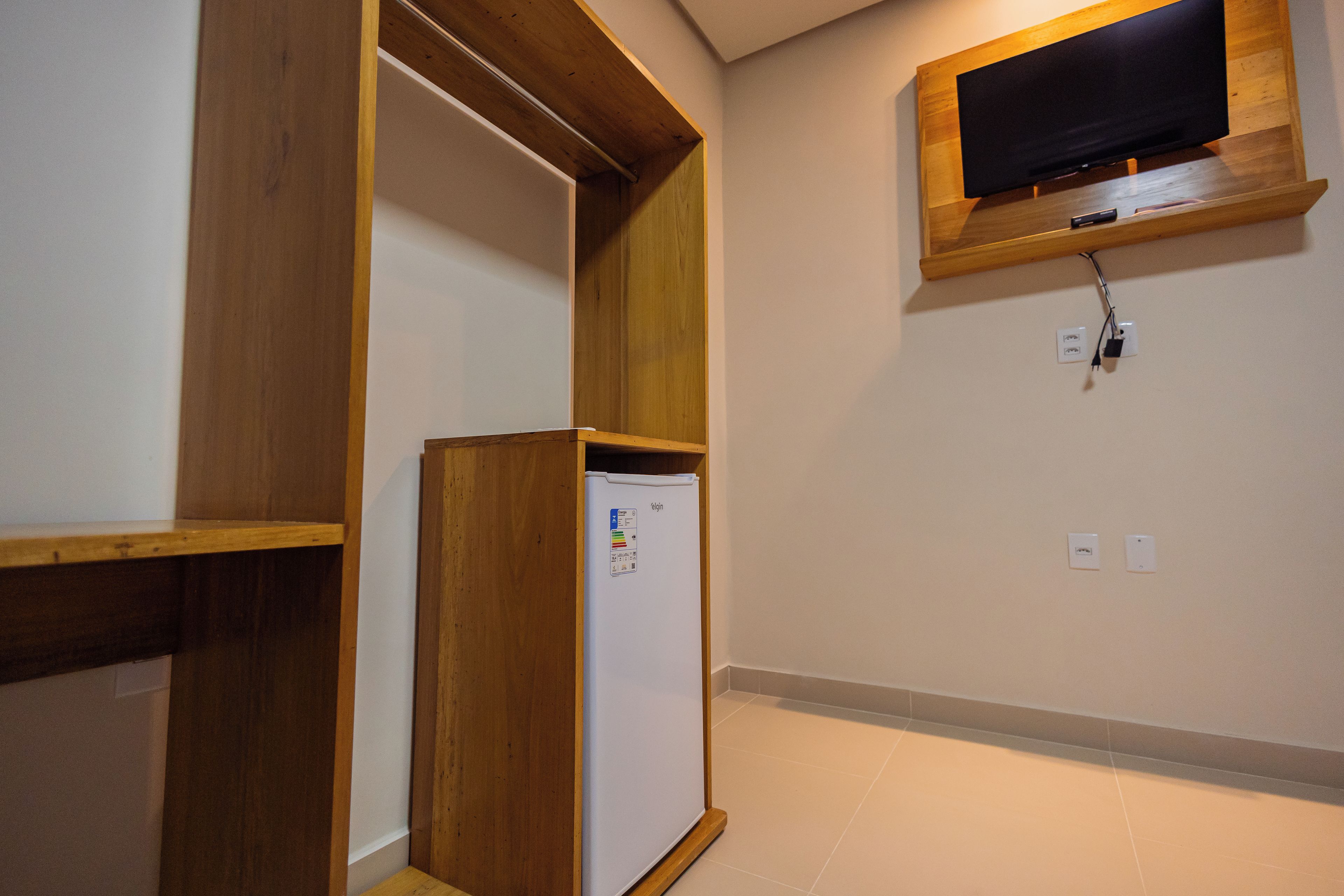 A room with a built-in wooden shelf, a white wall-mounted television, and a white refrigerator.