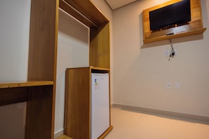 Quarto com prateleira de madeira embutida, televisão branca montada na parede e frigorífico branco.