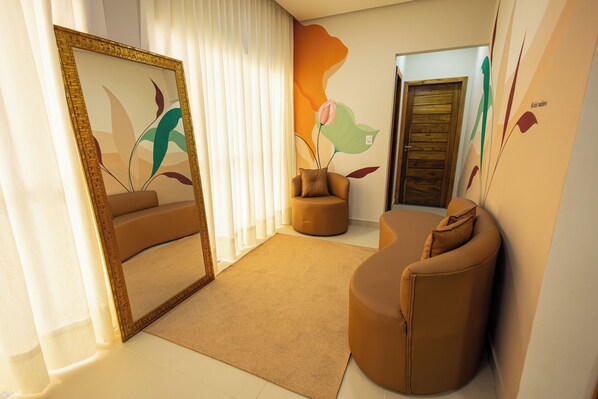 A modern interior with a large mirror, a sofa, a round ottoman, and a door with a wooden panel.