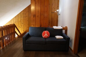 Ein dunkel gefärbtes Sofa mit einem roten und weißen Friedenssymbol-Kissen, einem weißen Handtuch und einer Holztreppe mit Geländer.