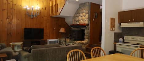 A cozy living room with a fireplace, wooden walls, a television, and a dining area with chairs and a table.