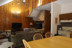 Ein gemütliches Wohnzimmer mit Kamin, Holzwänden, Fernseher und einem Essbereich mit Stühlen und Tisch.