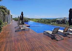 A wooden deck with a pool and lounge chairs overlooking a beach. - 3BR Playacar 3rd Floor - Rooftop Pool, Gym, Gated 24/7 (Playa del Carmen)