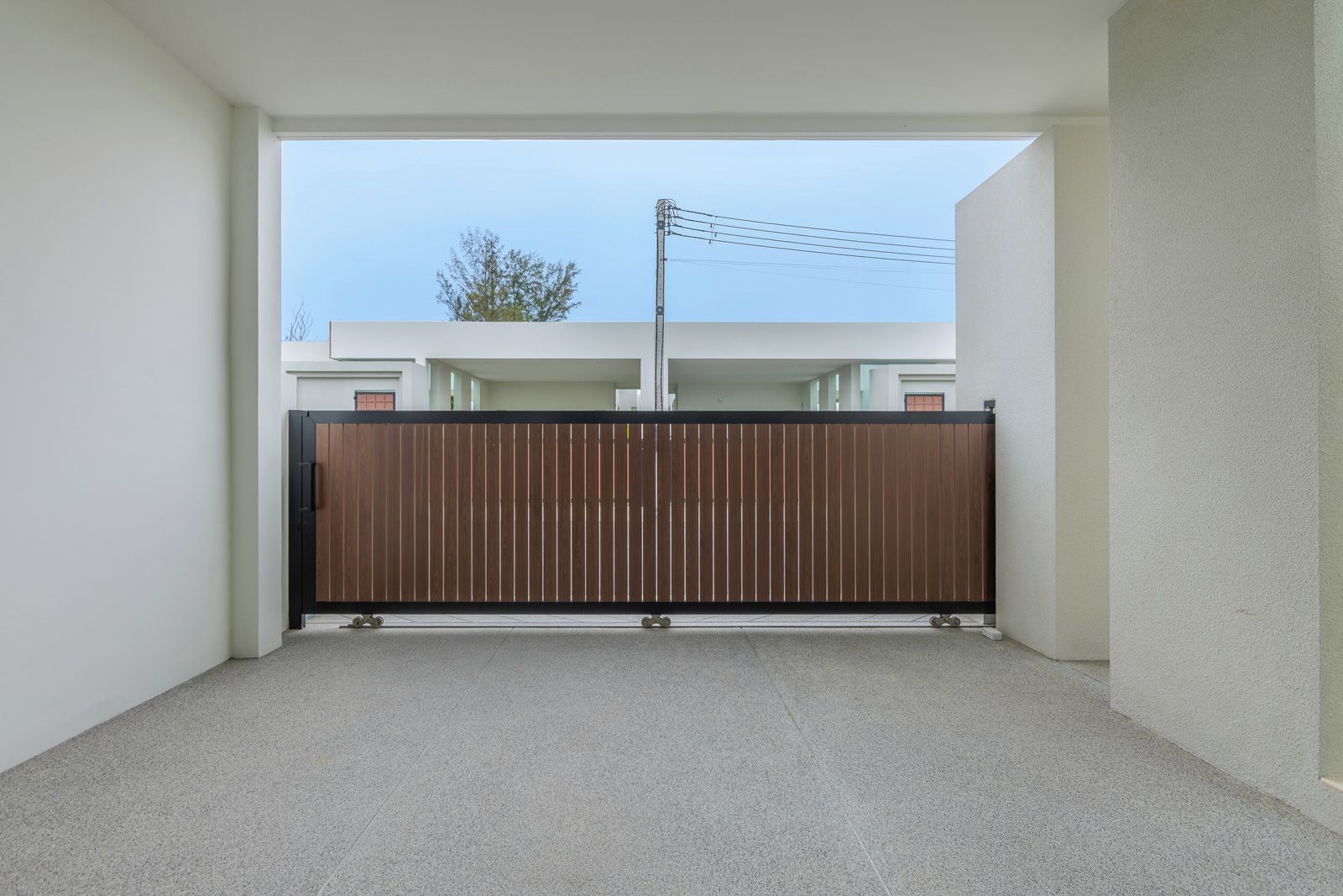 A narrow corridor with a wooden gate leading to a building with a visible power line.