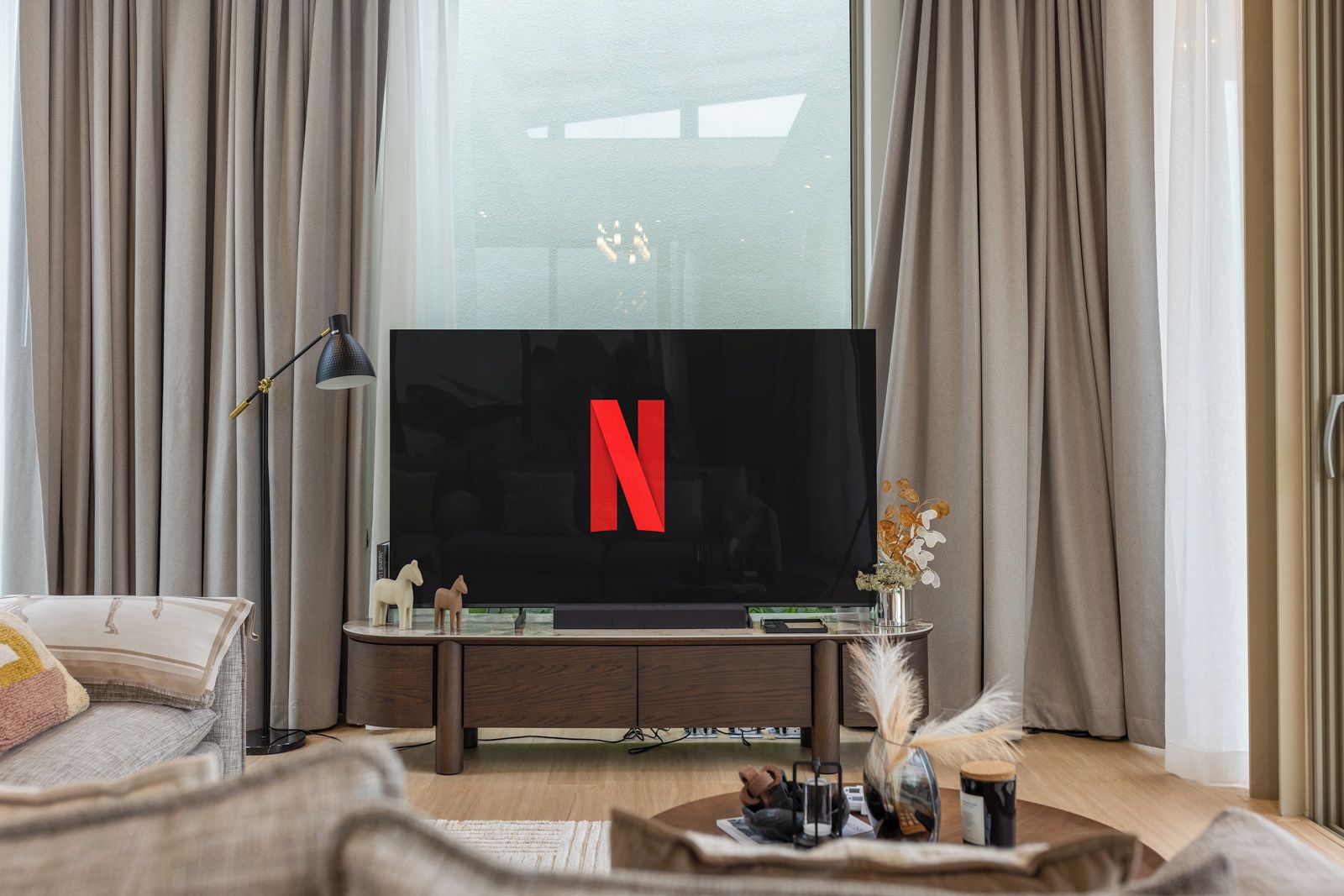 A modern living room with a flat-screen TV, a wooden entertainment unit, and a large window with curtains.