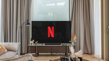 A modern living room with a flat-screen TV, a wooden entertainment unit, and a large window with curtains.