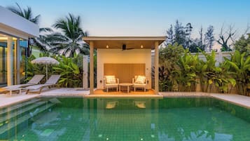 A modern outdoor pool area with lounge chairs and a covered seating area.