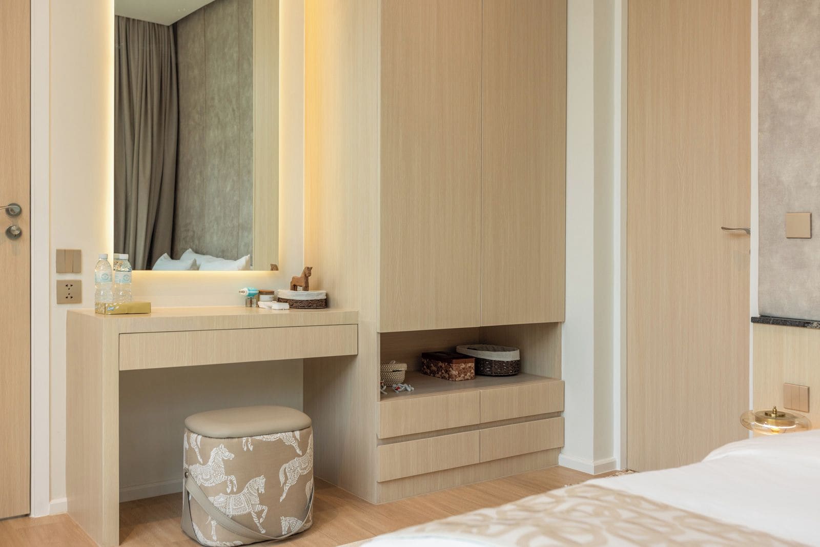 Un dormitorio moderno con un tocador de madera, un espejo, una mesita de noche y un taburete pequeño.