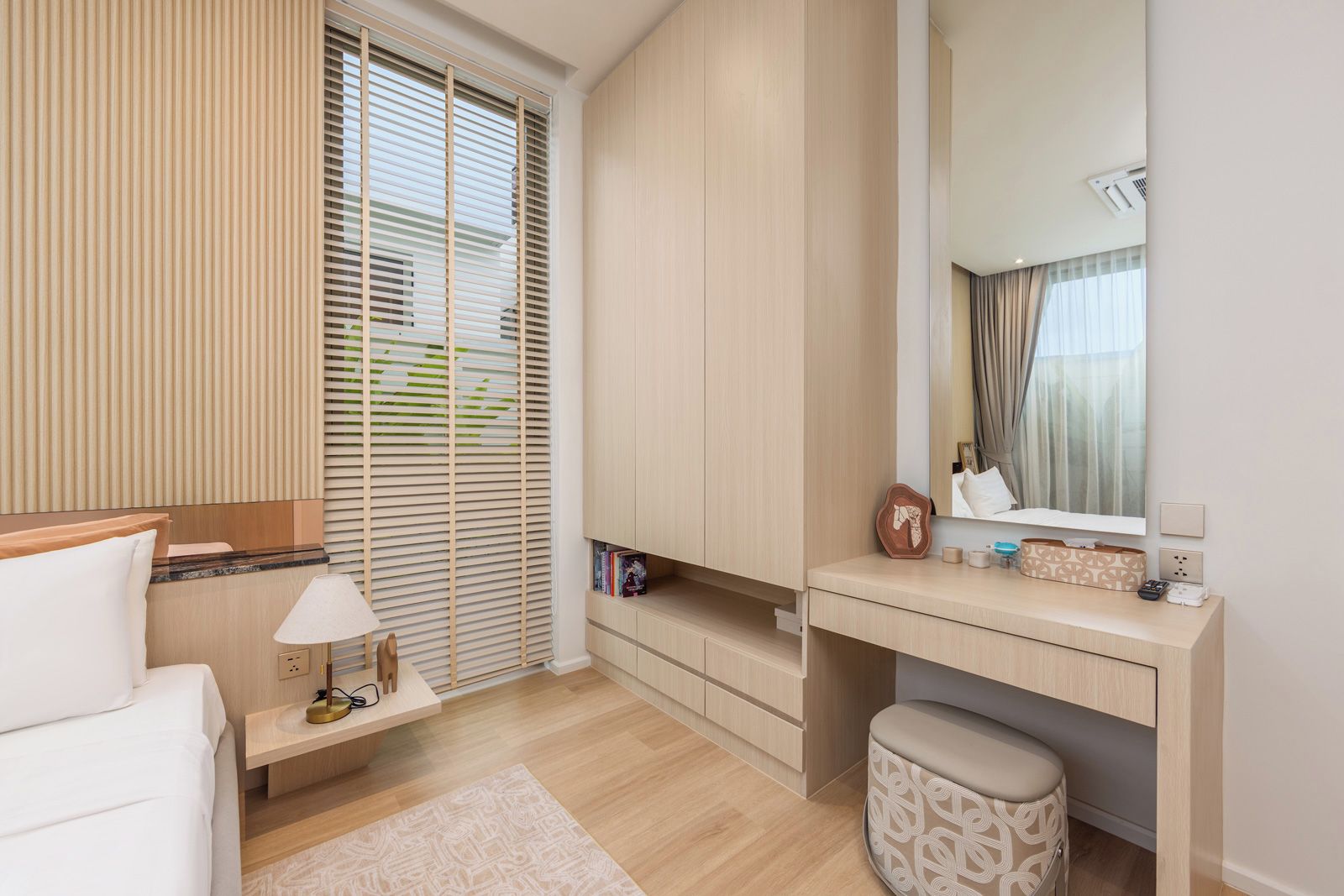 A modern bedroom with a bed, bedside table, lamp, and a desk with a mirror.