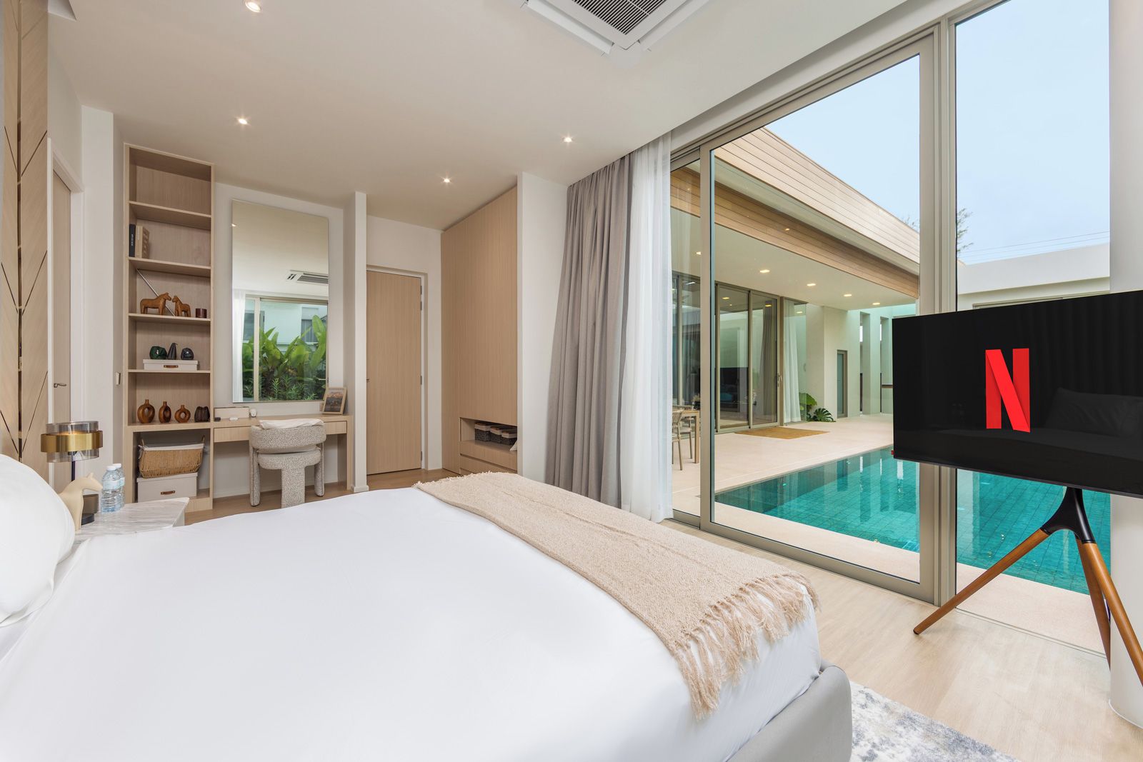 A modern bedroom with a large bed, a desk, and a TV screen displaying the Netflix logo.