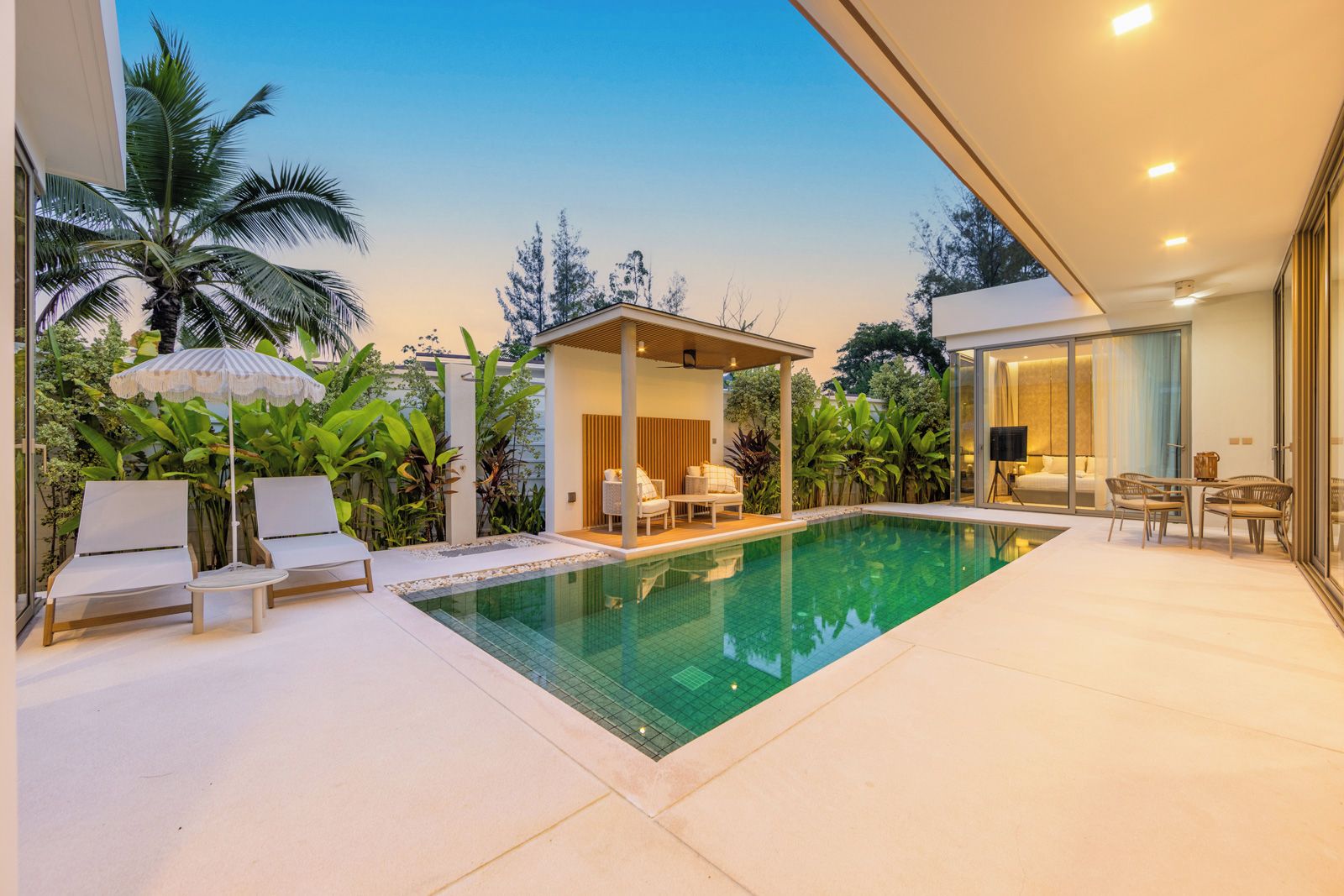 A modern poolside area with lounge chairs, a covered seating area, and a glass-enclosed bedroom.