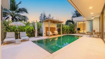 A modern poolside area with lounge chairs, a covered seating area, and a glass-enclosed bedroom.