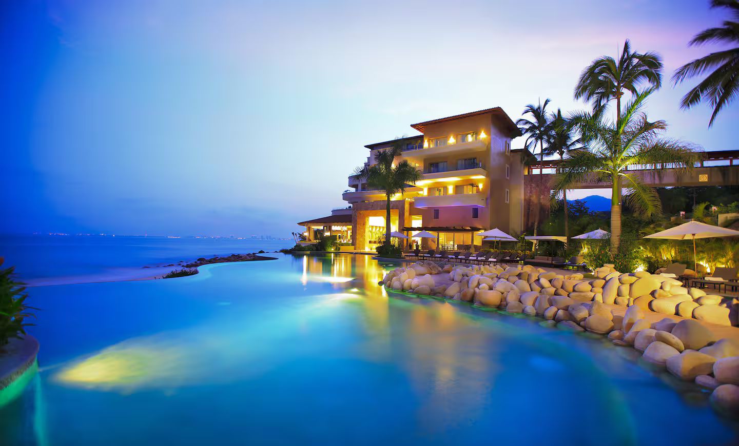 A resort with a pool, palm trees, and a building with multiple balconies.