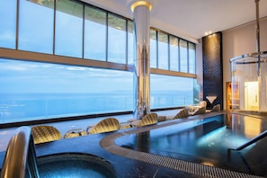 Un espace piscine intérieur moderne, doté de sièges et offrant une vue sur l’océan.
