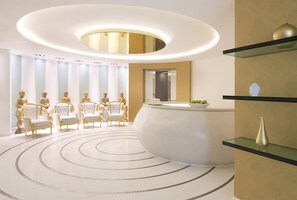 Un'area di accoglienza moderna con una disposizione di posti a sedere circolare, una reception e un vaso decorativo su uno scaffale.
