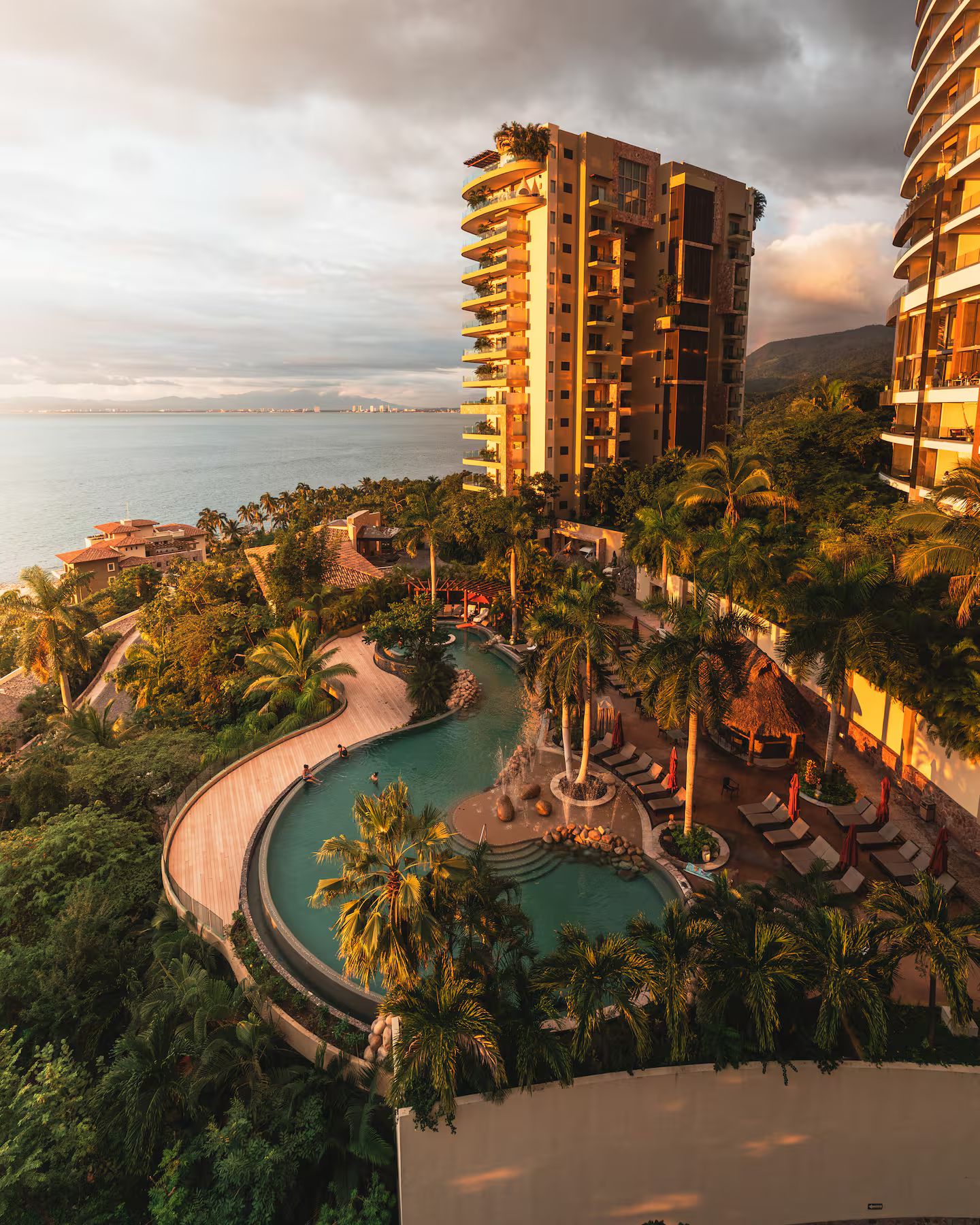 A resort with a pool, palm trees, and a view of the sea.