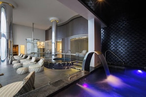 A modern spa area with a heated pool, lounge chairs, and a large column structure.
