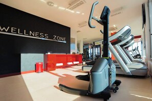 Ein Fitnessbereich mit Laufband, Ergometer und einem roten Empfangstresen.