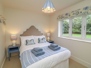 A bedroom with a bed, two bedside lamps, a window with a view, and a decorative ceiling light. - The Willows (Mablethorpe)