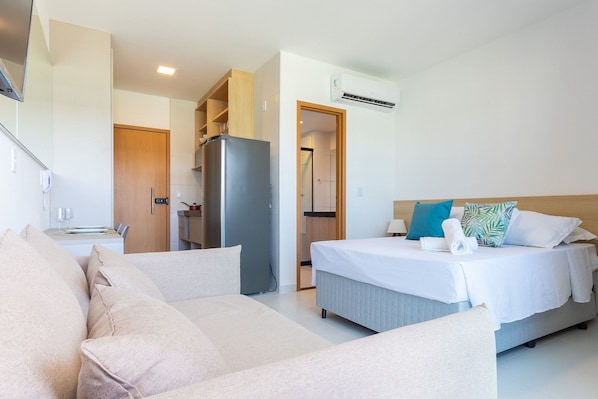 Quarto de hotel com cama, sofá, frigorífico e zona de cozinha.