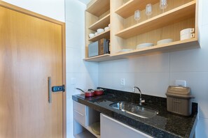 Uma cozinha com porta de madeira, bancada com pia e prateleiras com louças e copos.