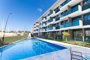 Un hotel moderno con piscina, varios balcones y un cielo azul despejado.