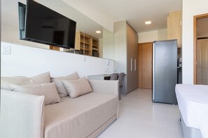 Een moderne woonkamer met een bank, een flatscreen televisie, een eethoek met een tafel en stoelen, en een inpandige keuken met een koelkast.