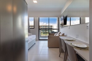 Een moderne hotelkamer met een bed, een sofa, een zithoek met een tafel en stoelen, en grote ramen met uitzicht op de stad.