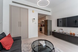 A modern living room with a sofa, a glass coffee table, a TV, and a kitchen in the background. - HAVN - Cozy Studio in Ghozlan, The Greens (Dubai)