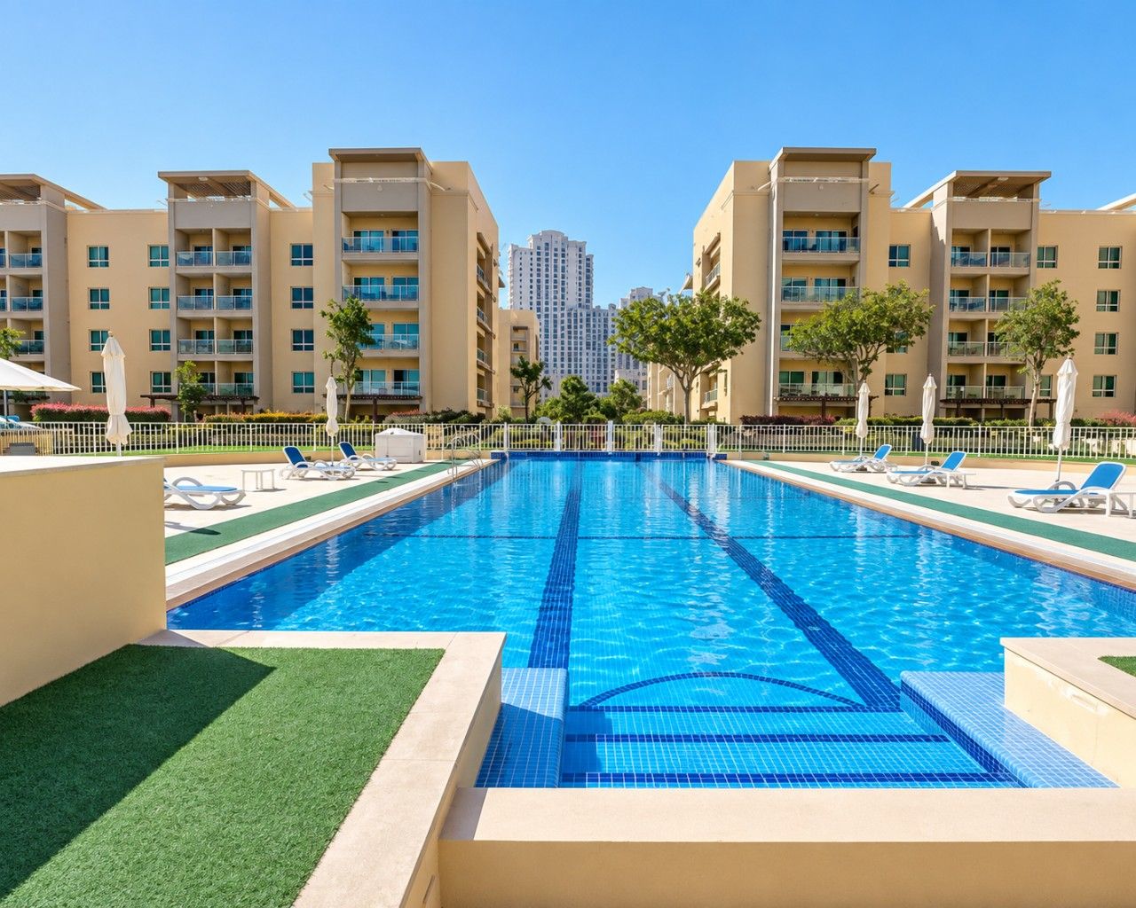 A swimming pool with a clear blue water, surrounded by lounge chairs and a white fence.