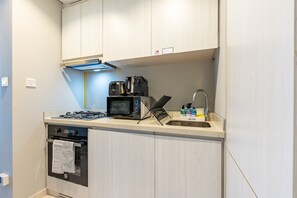 Eine kompakte Küchenzeile mit Gaskochfeld, Mikrowelle, Wasserkocher und einem kleinen Spülbecken, ausgestattet mit Reinigungsprodukten der Marke DELUXE.
